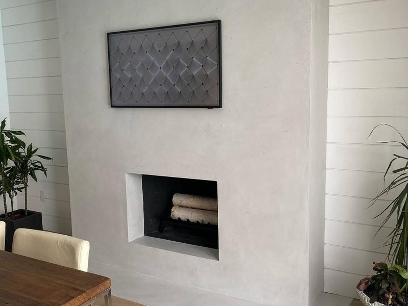 Seamless pale microcement fireplace surround running from floor to ceiling between white shiplap walls.