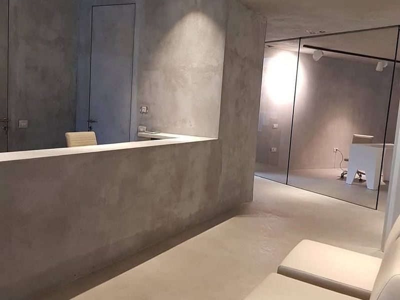 Reception counter and walls finished in mottled grey microcement, with a white worktop and a mirrored partition.