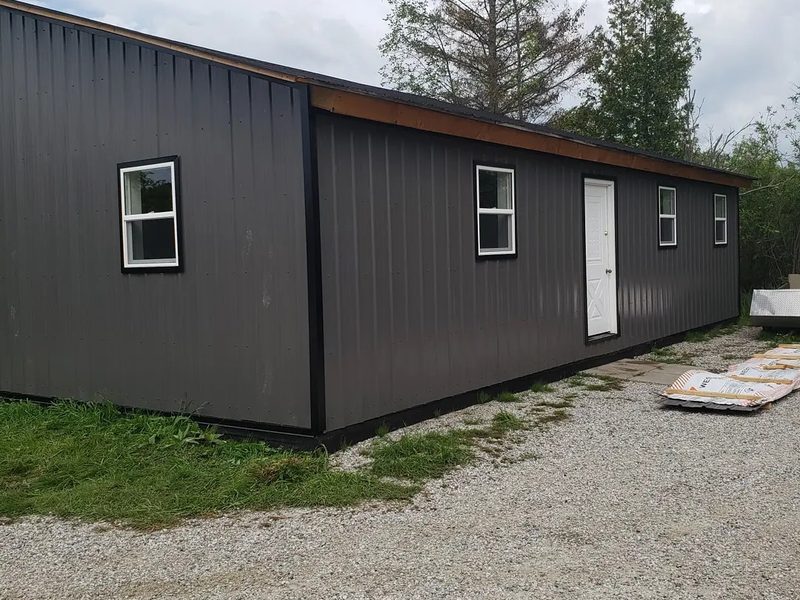 Long outbuilding clad in dark vertical steel panels with white-framed windows and a white entry door.