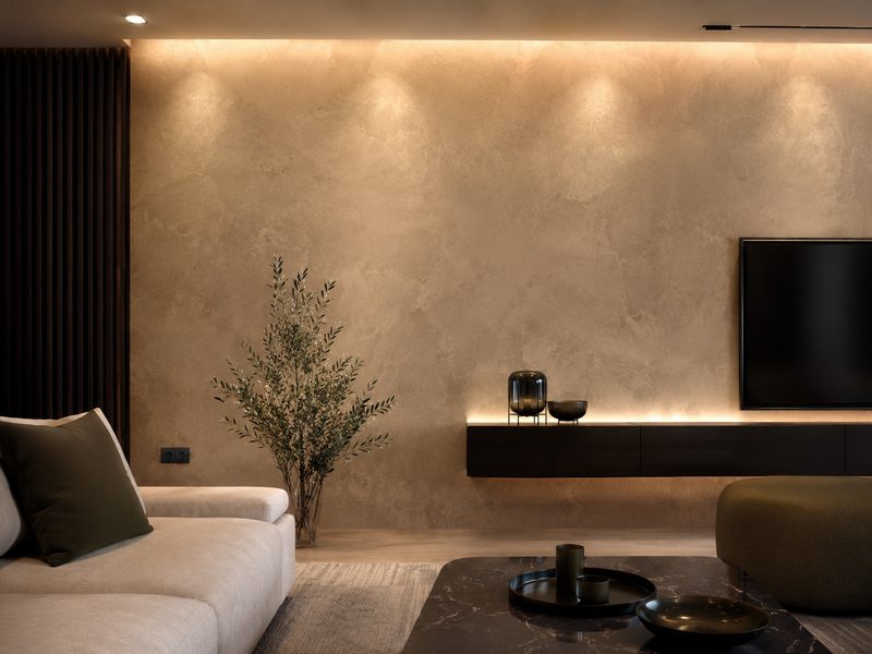 Warm Venetian plaster wall lit from above by downlights, with a dark floating cabinet and a television mounted on it.