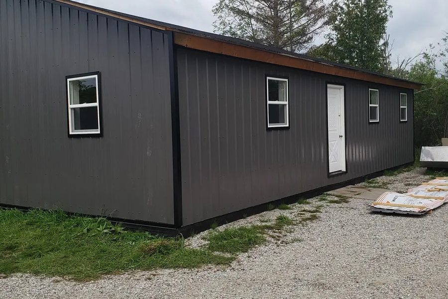 Long steel-clad outbuilding with dark vertical metal panels and a new metal roof edge.