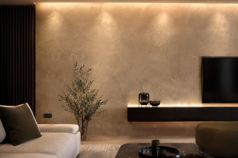 Living room with a warm polished plaster feature wall lit from above by recessed downlights.